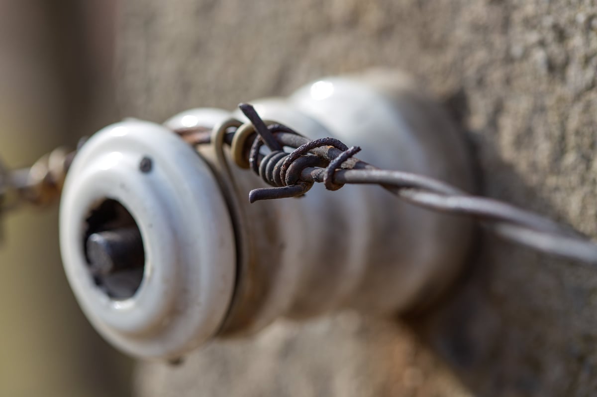 Rusty vintage porcelain electrical insulator with twisted metal wires on concrete wall — CN Electrical aluminum wiring inspection and remediation in Chilliwack, BC