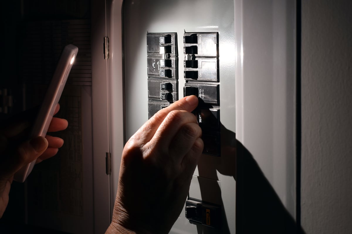 Closeup of person checking residential circuit breakers with smartphone flashlight during home electrical work — CN Electrical panel load calculation and EV charger assessment in Chilliwack, BC