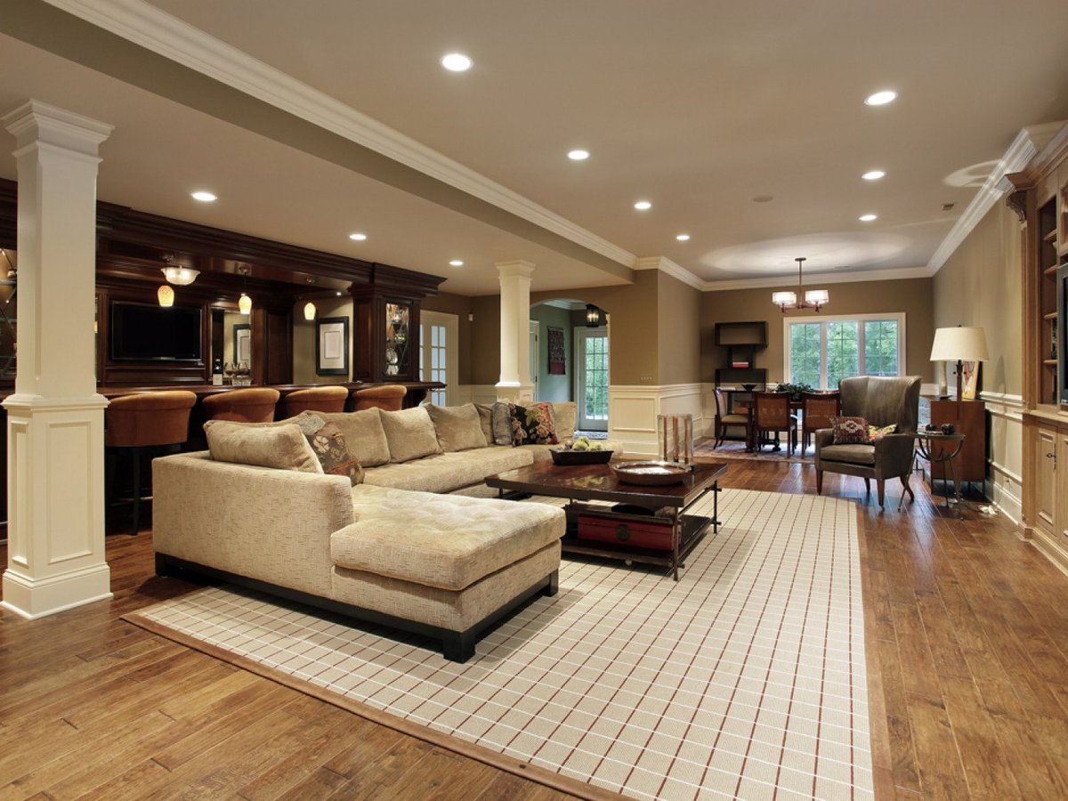 Luxury finished basement with cream sectional sofa, dark wood bar, recessed lighting, white columns, and mixed flooring