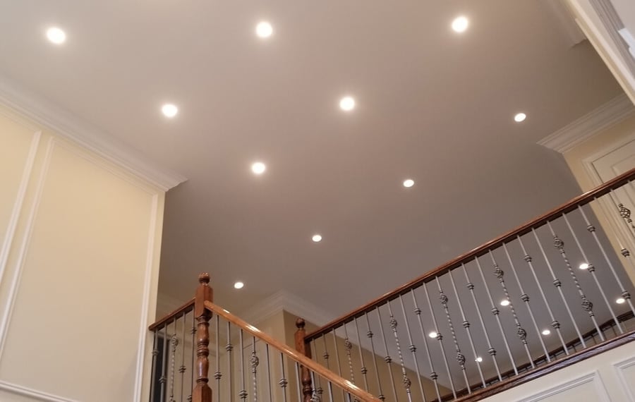 Staircase landing with wooden railings and recessed ceiling lights in a modern home interior