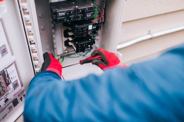 Electrician in red gloves working on an electrical circuit breaker panel with blue protective sleeve visible